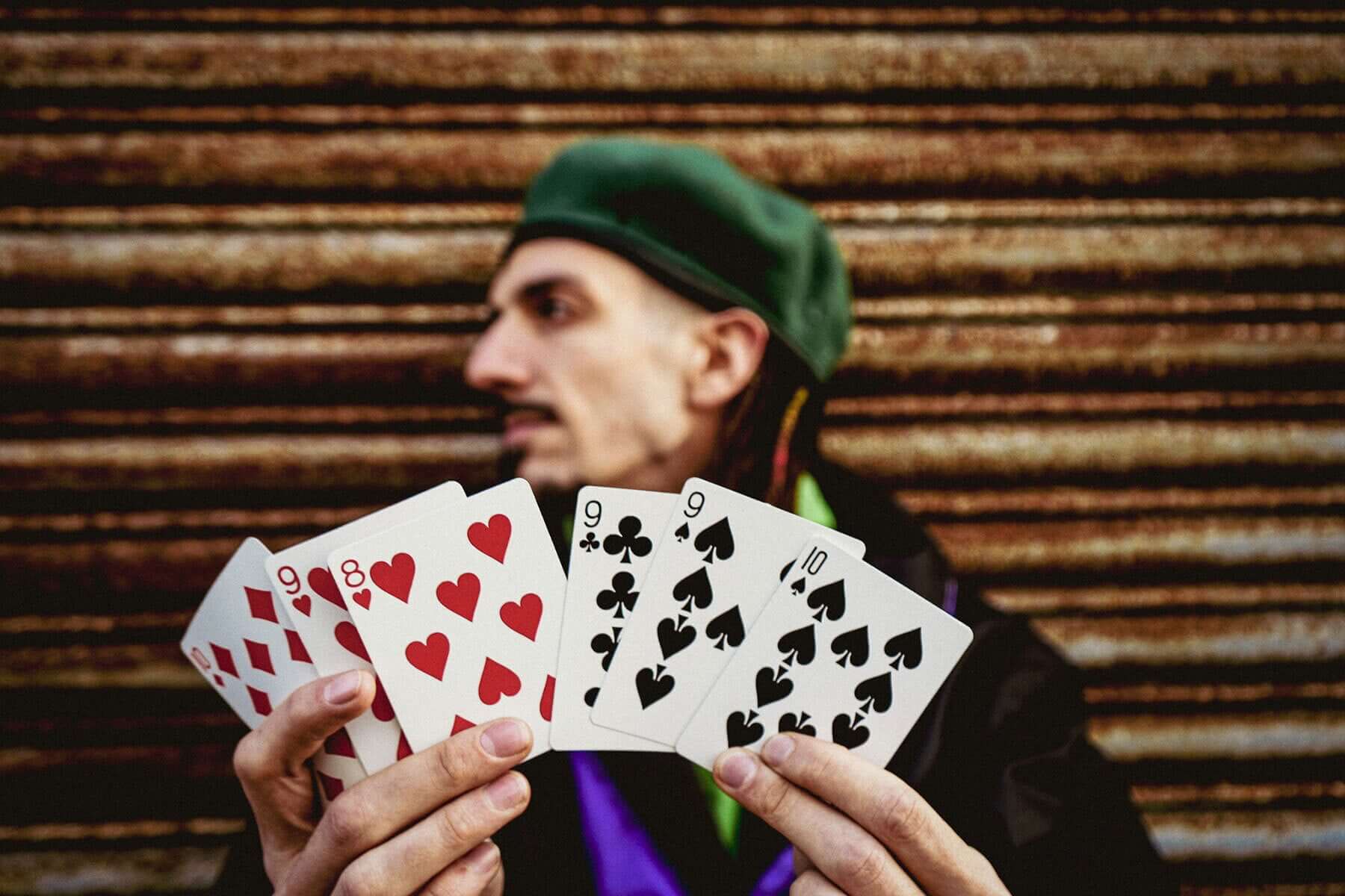 A magician holding playing cards demonstrating the magic trick H2O against a rustic background.