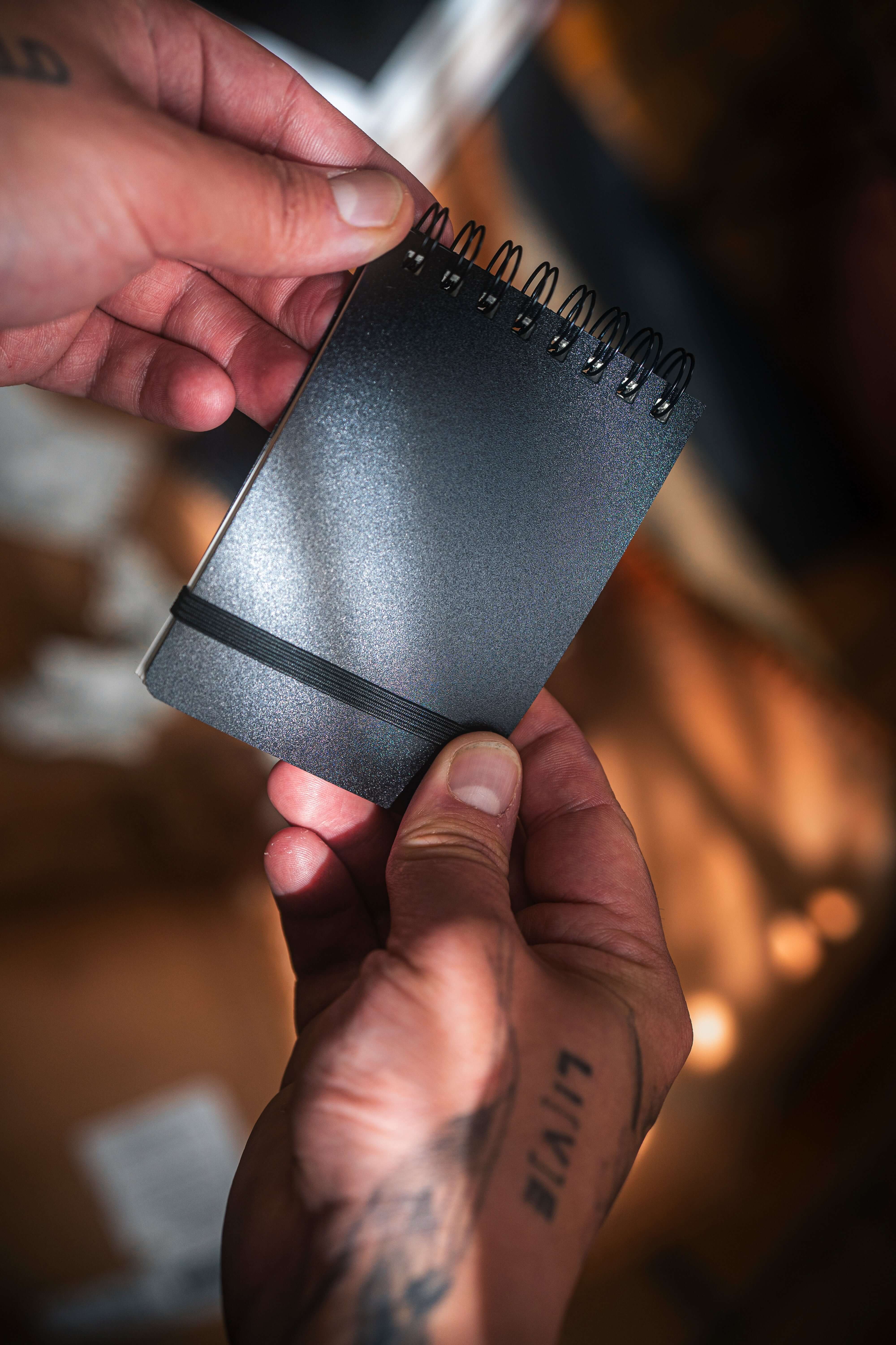 REPLICA: Pocket-size Impression Pad held in hands, showcasing its sleek black design and spiral binding.